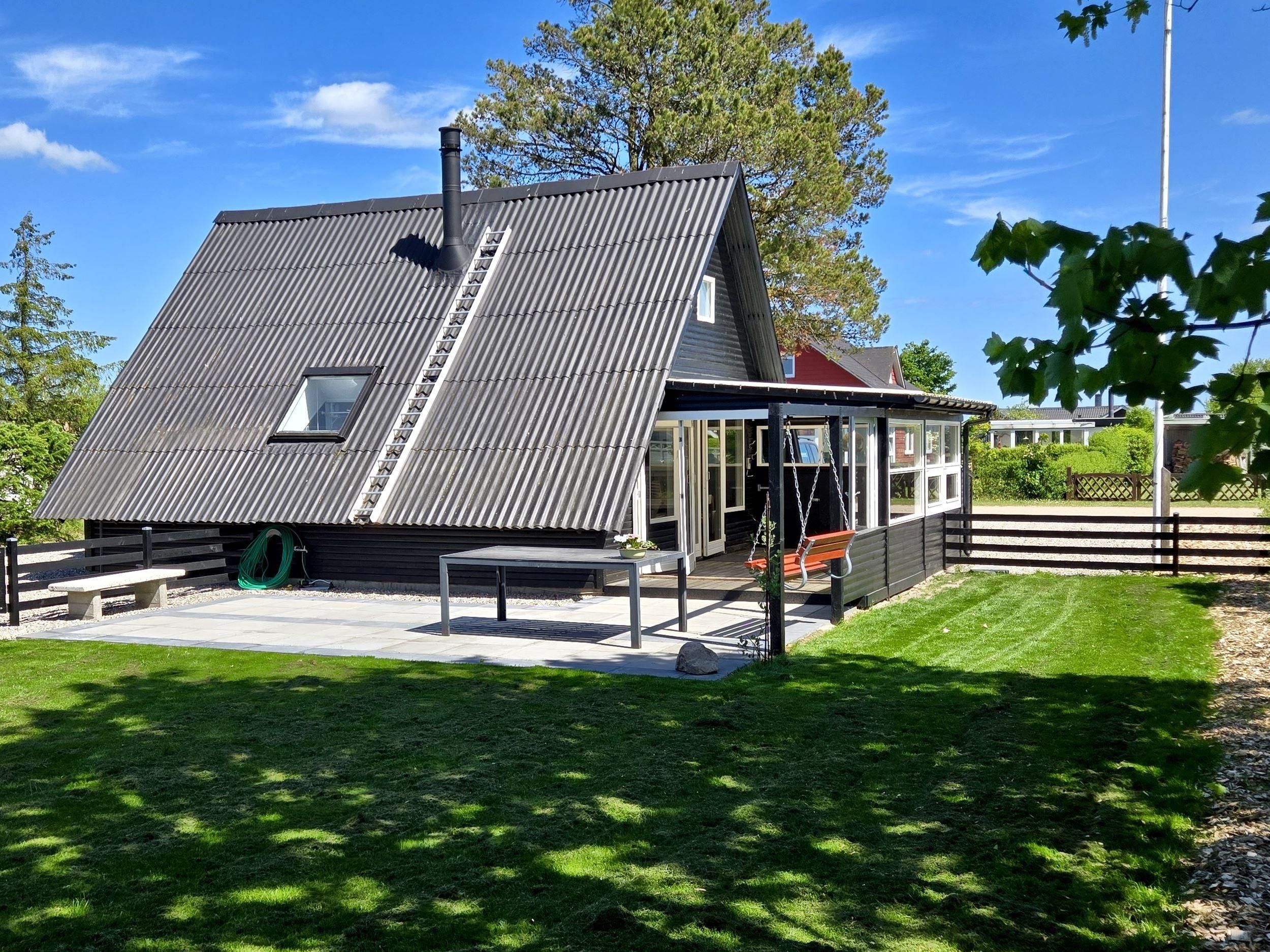 Una casa moderna con techo inclinado, una chimenea visible y un pequeño porche con una mecedora.