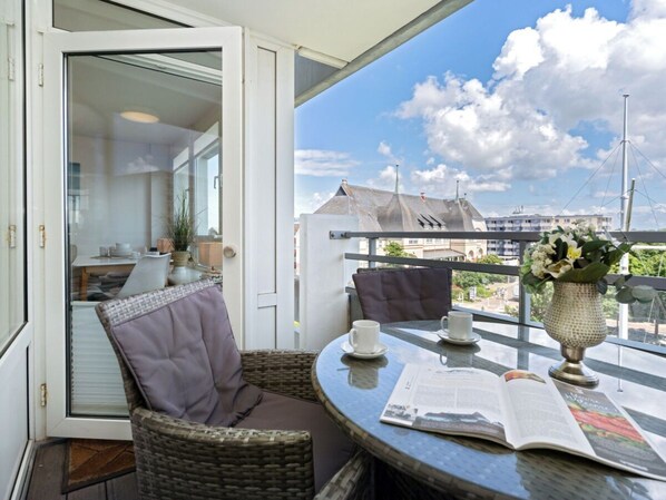 A balcony with wicker furniture, a table with a newspaper, and a vase with flowers. - Holiday Apartment With 2 Bedrooms (Sylt)