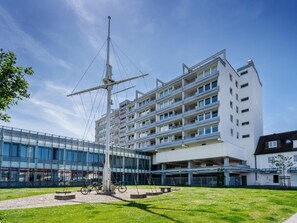 A modern building with multiple floors, a central flagpole, and a grassy courtyard with bicycles. - Holiday Apartment With 2 Bedrooms (Sylt)