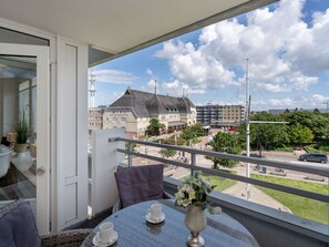 A balcony with a table and chairs, a vase of flowers, and a view of buildings and a street. - Holiday Apartment With 2 Bedrooms (Sylt)