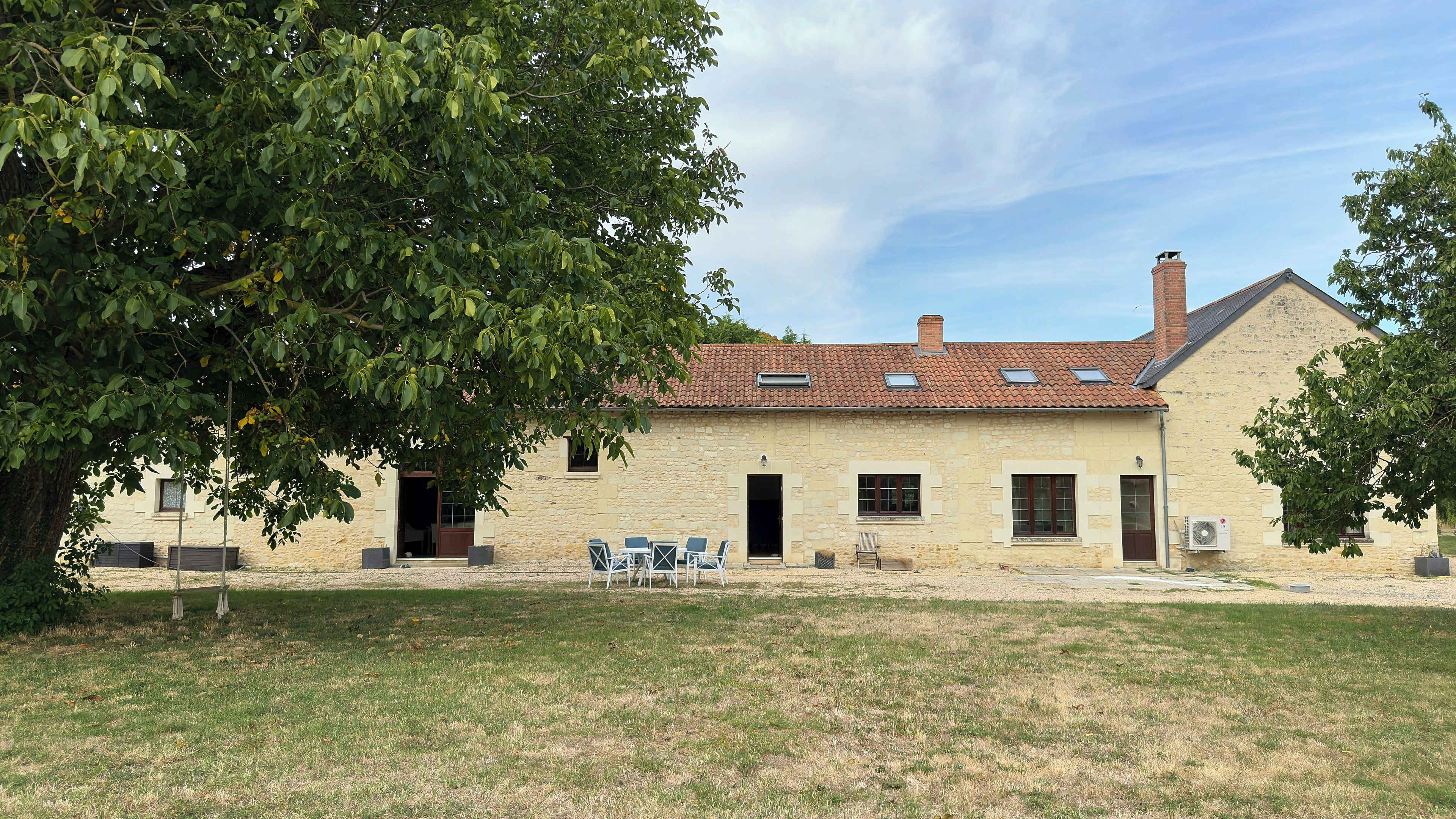 A stone building with a tiled roof, a grassy lawn, and outdoor seating.
