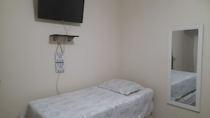 A small, single-bed room with a television mounted on the wall, a power strip, and a mirror. - New Listing (Guarujá)