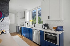 A modern kitchen with white and blue cabinets, stainless steel appliances, and a large window providing natural light. - Blue Horizon at Longboat Key - 2 bedroom condo with spectacular views (Longboat Key)