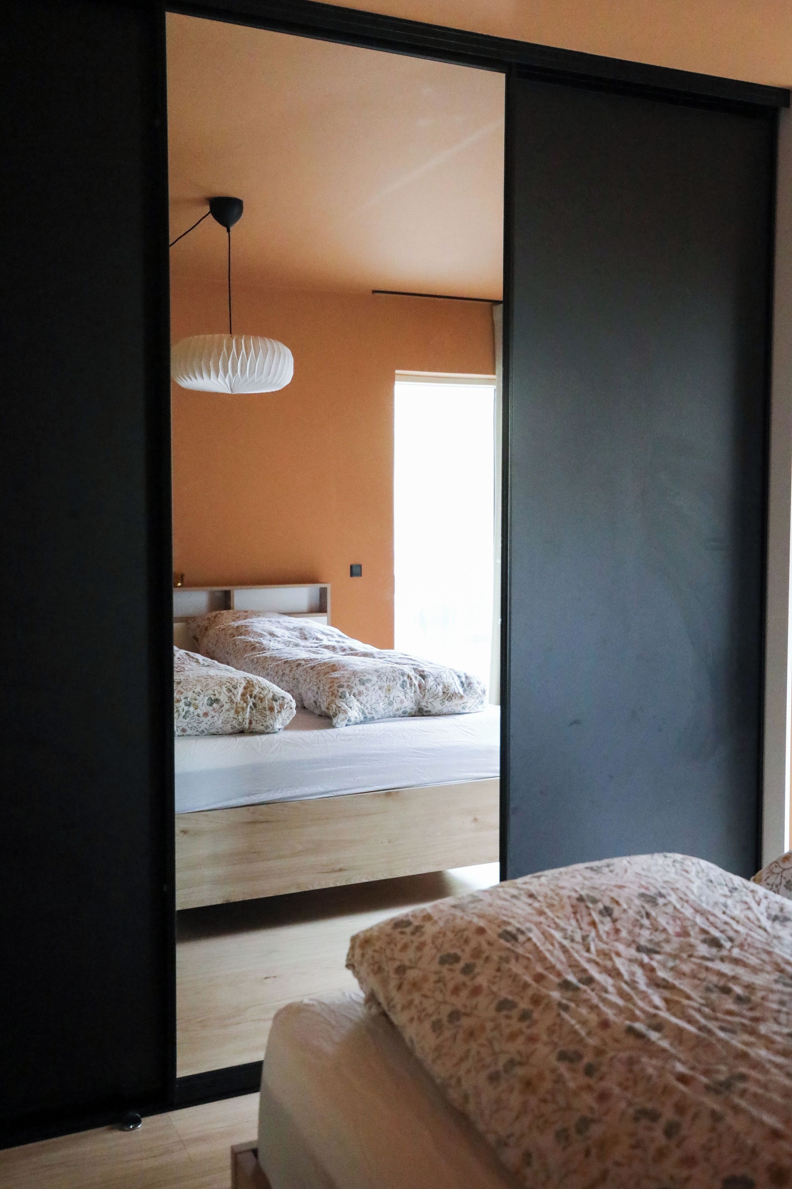 A bedroom with a bed, a hanging light fixture, and a view through an open door.