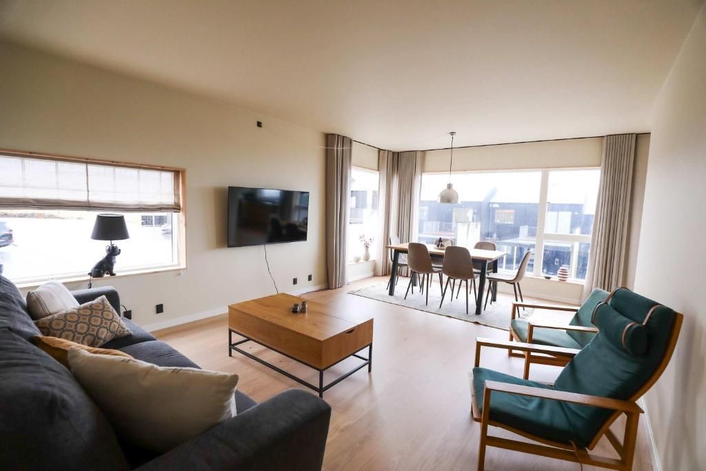 Una sala moderna con un sofá, una mesa de centro y un televisor montado en la pared. Hay un comedor con una mesa y sillas.