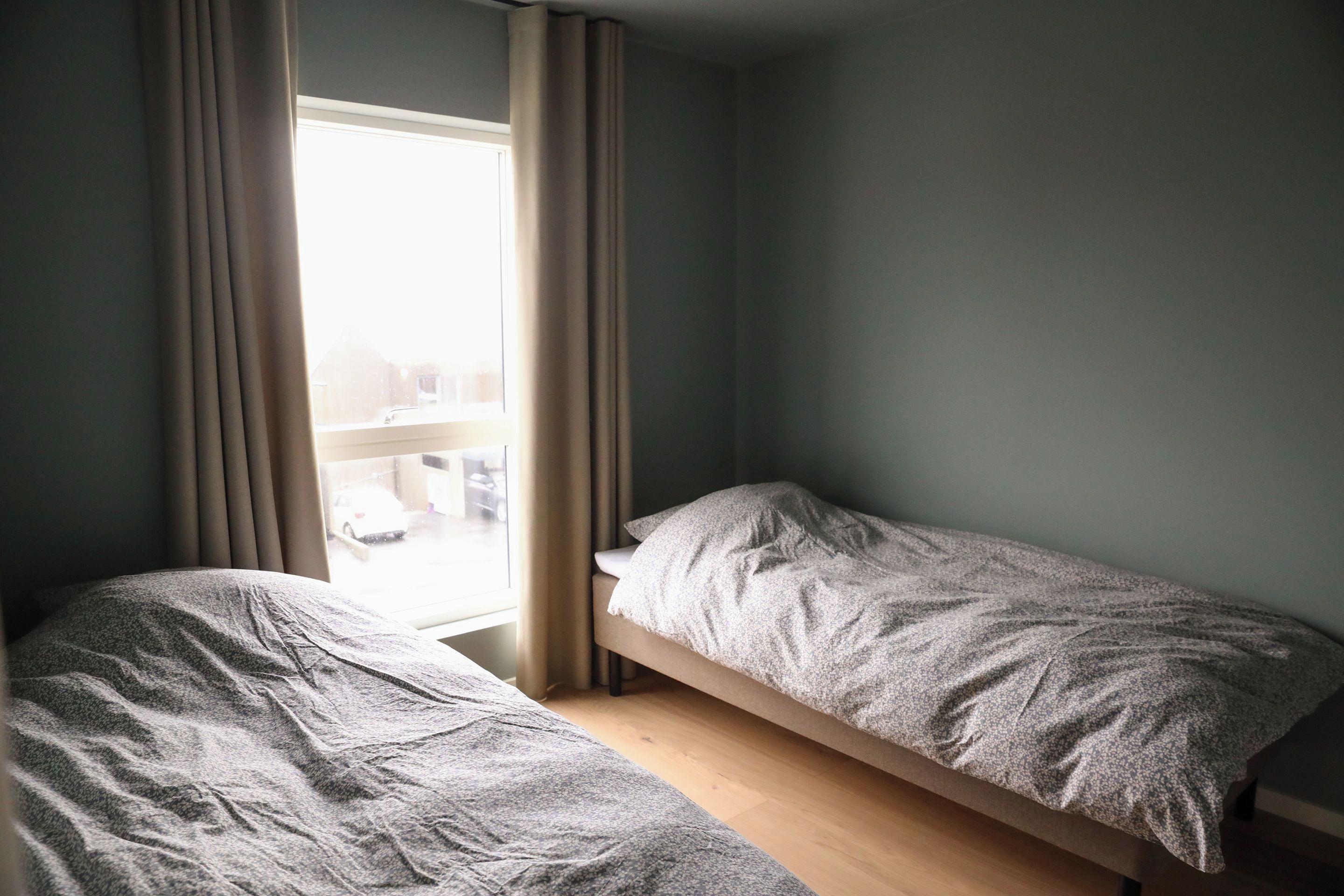 A small, single-bed room with a window, curtains, and a view of a snowy landscape.