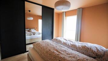 Een slaapkamer met een bed, een spiegel, een hanglamp en een raam met gordijnen.