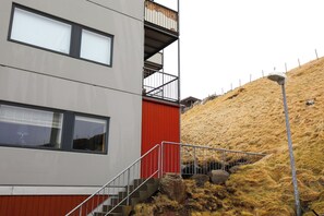 A modern building with a red and grey facade, a balcony, and a staircase leading to the entrance. - UK 39, 1. TV (Argir)
