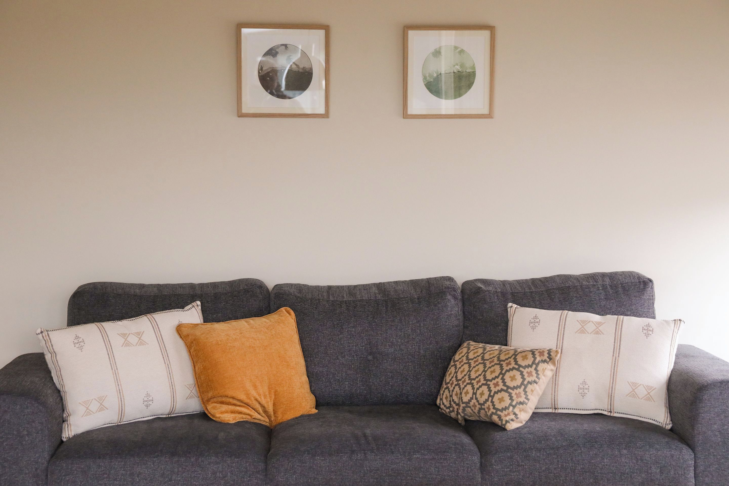 A grey sofa with patterned cushions and two framed pictures on the wall.