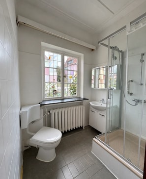 Ein Badezimmer mit Toilette, Waschbecken, Dusche und einem Fenster mit Blick auf Gebäude.