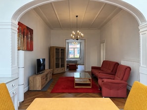 Ein Wohnzimmer mit Fernseher, einem roten Sofa, einer Holzkommode und einem roten Teppich.