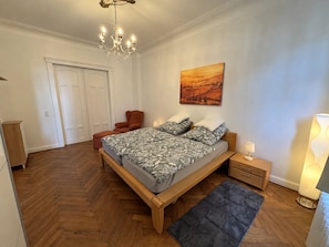 Ein Schlafzimmer mit einem hölzernen Bett, einem Nachttisch, einem Sessel, einem Gemälde und einer Chandelier.