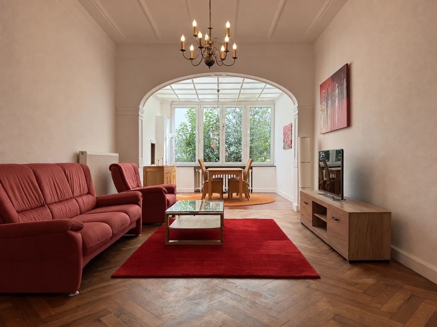 A living room with a red sofa, a glass coffee table, a wooden cabinet, and a TV.