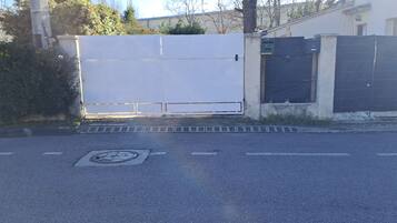 Een toegangshek met een metalen poort, een betonnen pad en een putdeksel in de weg.