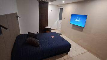Een slaapkamer met een bed, een aan de muur bevestigde televisie waarop het Disney+-logo te zien is, en een klein nachtkastje.