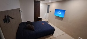 Une chambre à coucher avec un lit, un téléviseur fixé au mur affichant le logo de Disney+, et une petite table de chevet.