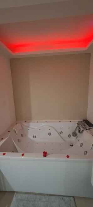 Une baignoire avec une lumière rouge au-dessus, une serviette et une petite décoration en forme de cœur rouge.