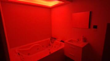 Une salle de bain éclairée de lumière rouge, avec une baignoire, un lavabo et un miroir.