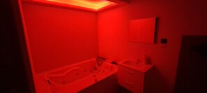 Une salle de bain éclairée de lumière rouge, avec une baignoire, un lavabo et un miroir.