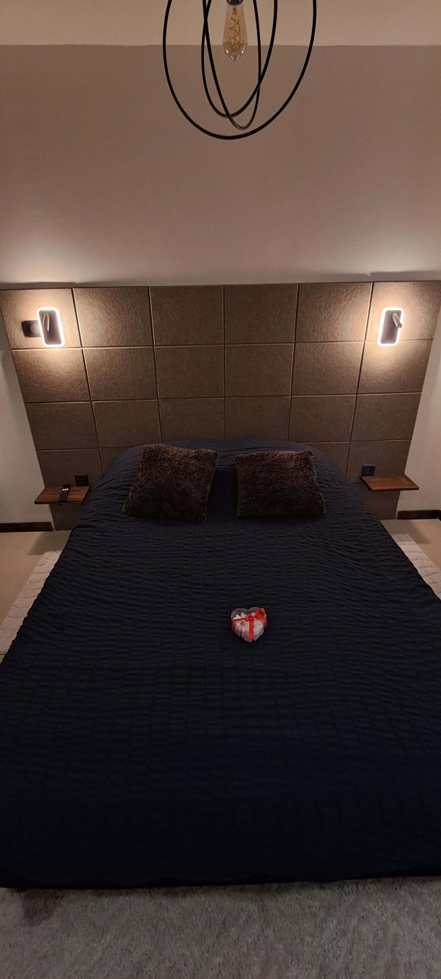 Une chambre à coucher avec un grand lit, deux tables de chevet et un luminaire moderne au-dessus.