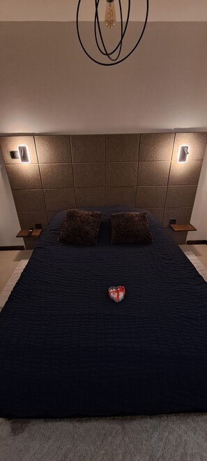 Une chambre à coucher avec un grand lit, deux tables de chevet et un luminaire moderne au-dessus.