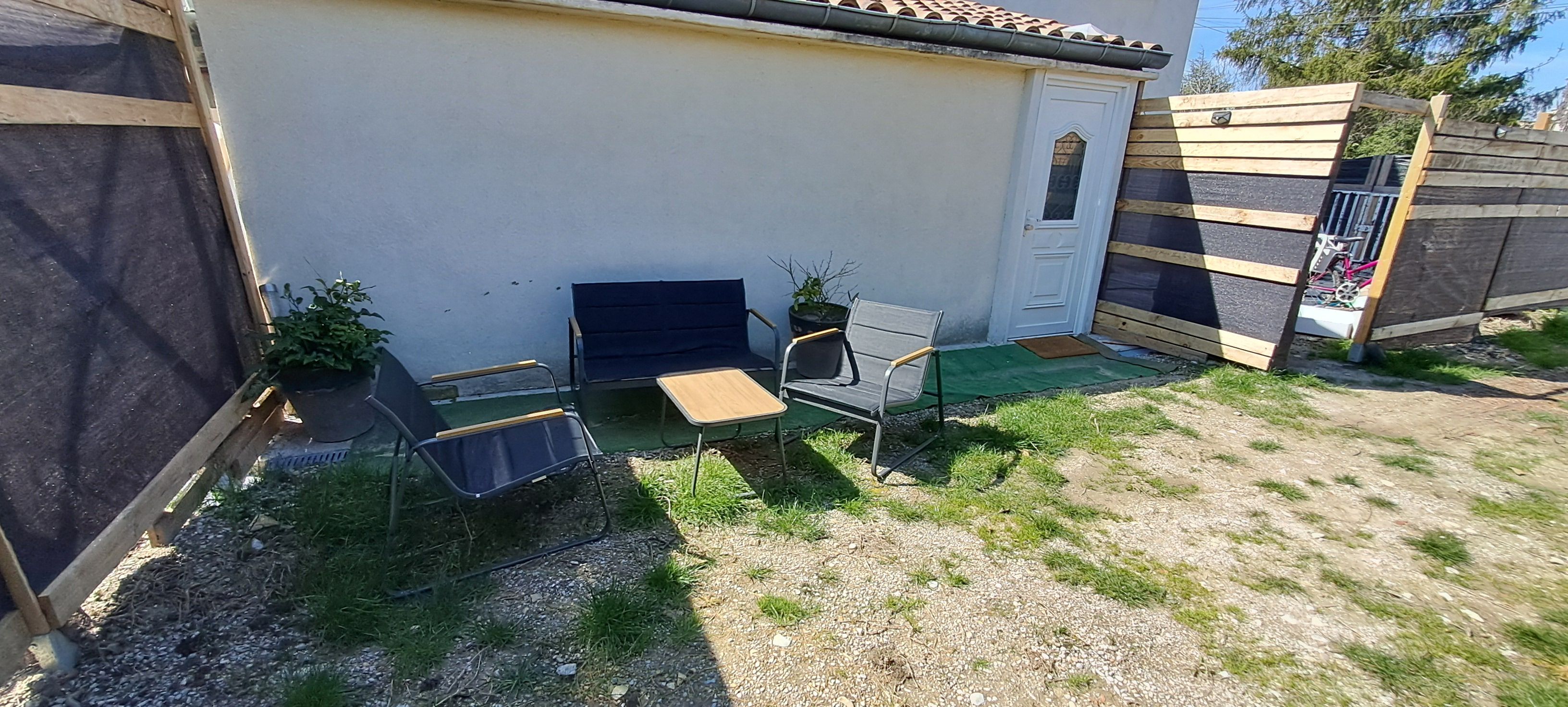 Een omheind buitengebied met een tafel, stoelen, een deur en een kleine tuin.