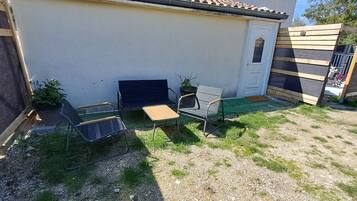 Een omheind buitengebied met een tafel, stoelen, een deur en een kleine tuin.
