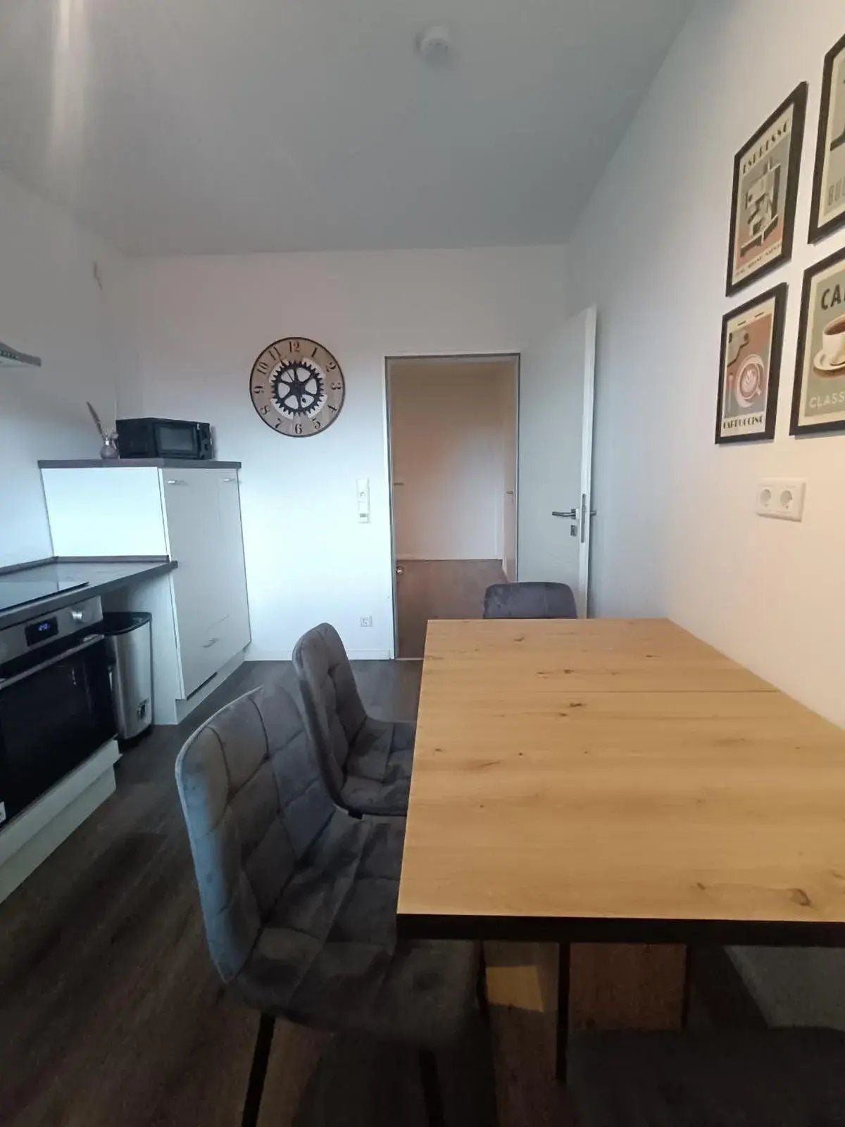 Eine kleine Küche mit einer Mikrowelle, einer Uhr und einem Kühlschrank. Ein Esstisch mit einem Stuhl steht davor.