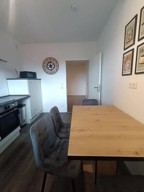 Cozinha compacta com micro-ondas, relógio e geladeira. Há uma mesa de jantar com uma cadeira em frente.