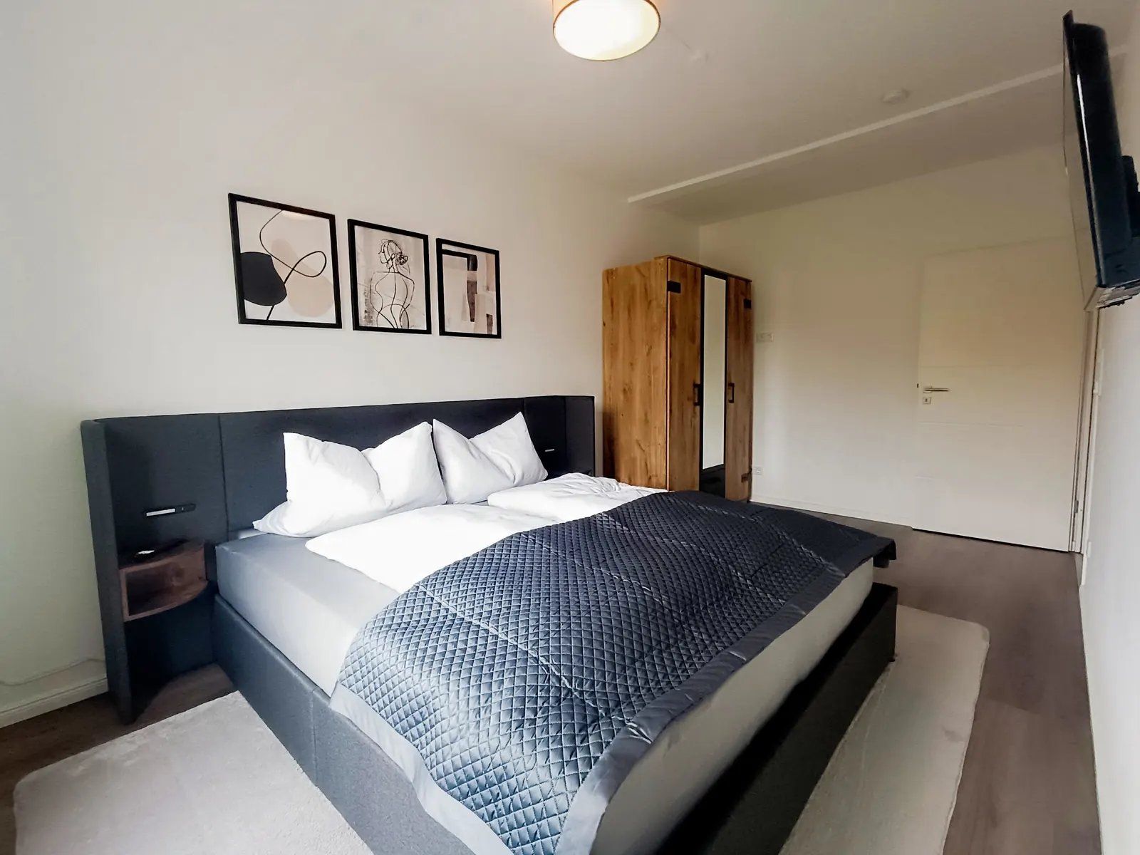 Ein modernes Schlafzimmer mit einem großen Bett, einem Nachttisch, einem Kleiderschrank und einem an der Wand befestigten Flachbildfernseher.
