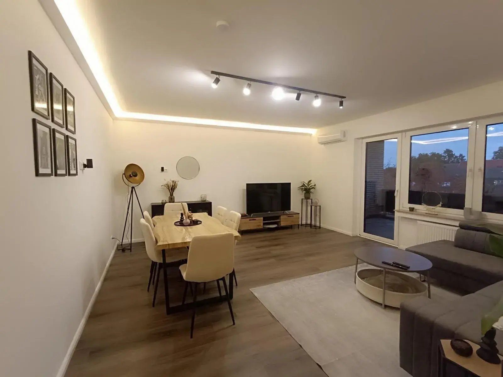 Ein modernes Wohnzimmer mit Essbereich, einem Flachbildfernseher und einem großen Fenster.