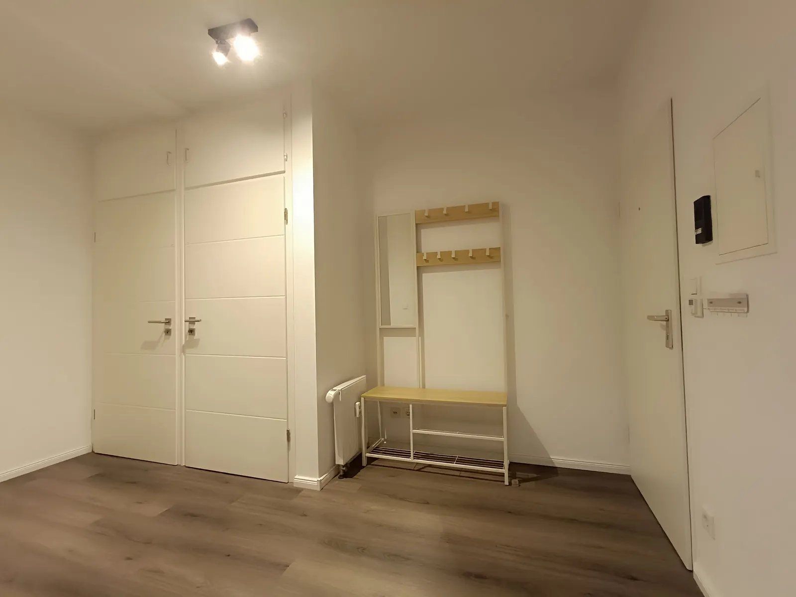 Ein Zimmer mit geschlossenem Kleiderschrank, einer Sitzbank und einem Heizkörper.