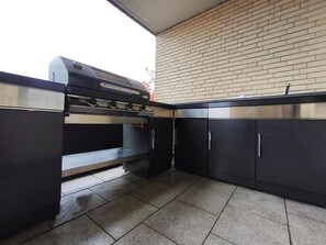 Une cuisine équipée d’un barbecue intégré, de meubles en acier inoxydable et d’un sol carrelé.