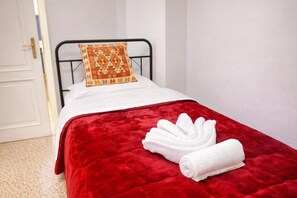 A single bed with a red quilt and a white pillow with a geometric pattern. - NEXT Palace (Roma)