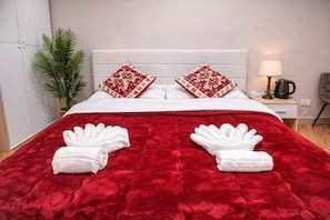 Un lit avec une couverture rouge, des oreillers blancs et deux serviettes blanches.