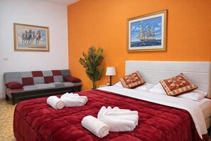 Quarto de hotel com uma cama grande, um sofá, uma planta em vaso e duas fotos emolduradas nas paredes.