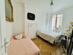A bedroom with two beds, a radiator, a window with a view, and a door. - New Listing (Paris)