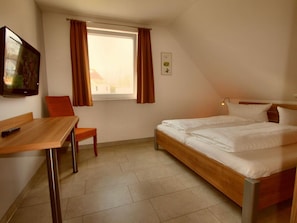 Una habitación pequeña y bien iluminada con una cama individual, un escritorio y una silla.