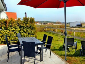 An outdoor patio with a table and chairs, a red umbrella, and a view of a rural landscape. - Holiday Home Fohlenweide (Goehren-Lebbin)