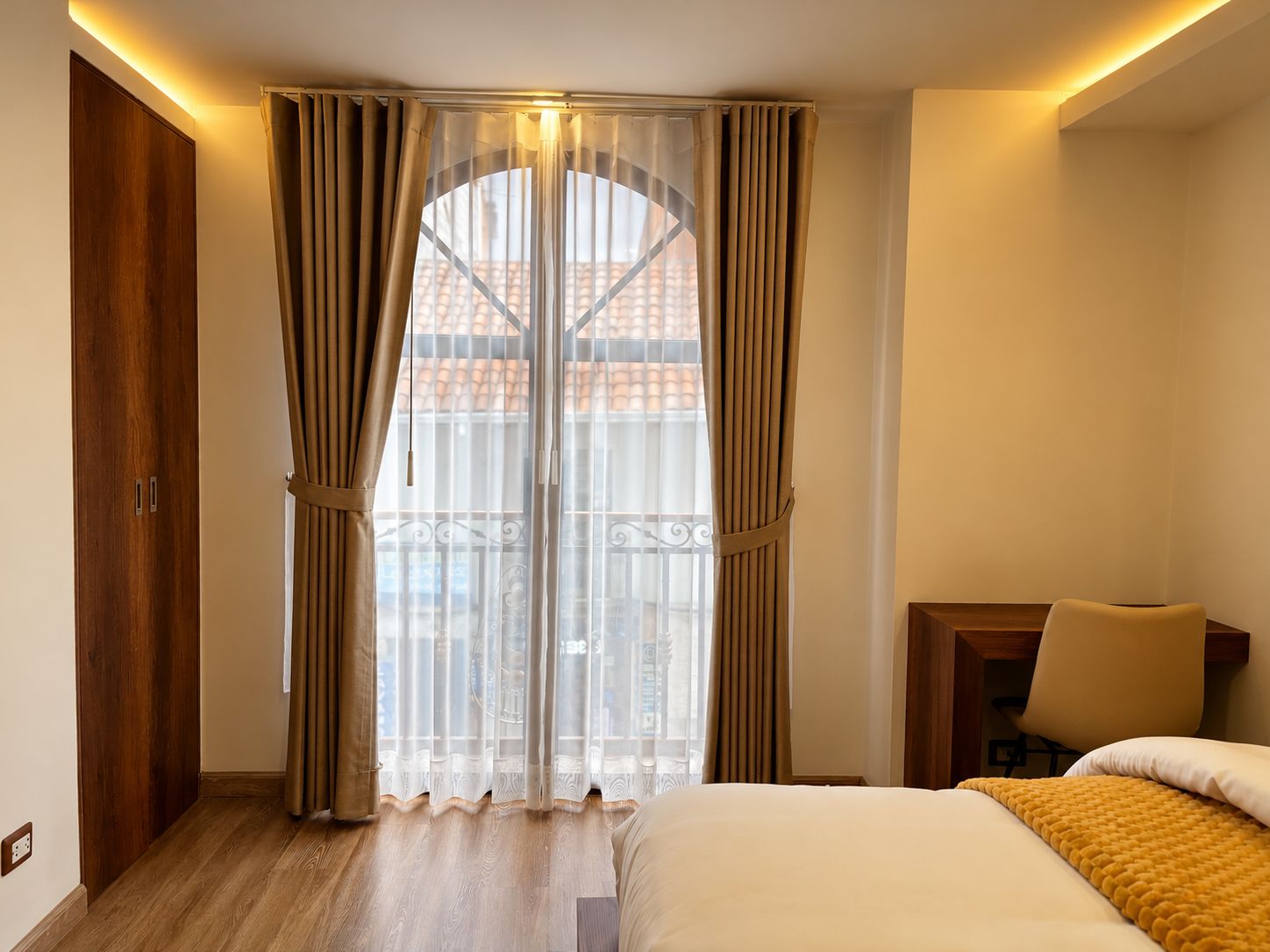 Ein Hotelzimmer mit Bett, Stuhl, Holzschrank und einem Balkon mit Blick auf Gebäude.