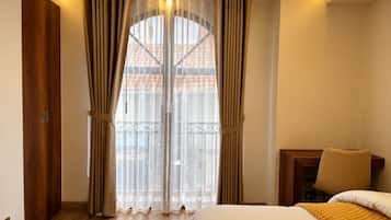 Una habitación de hotel con cama, una silla, un armario de madera y un balcón con vistas a edificios.