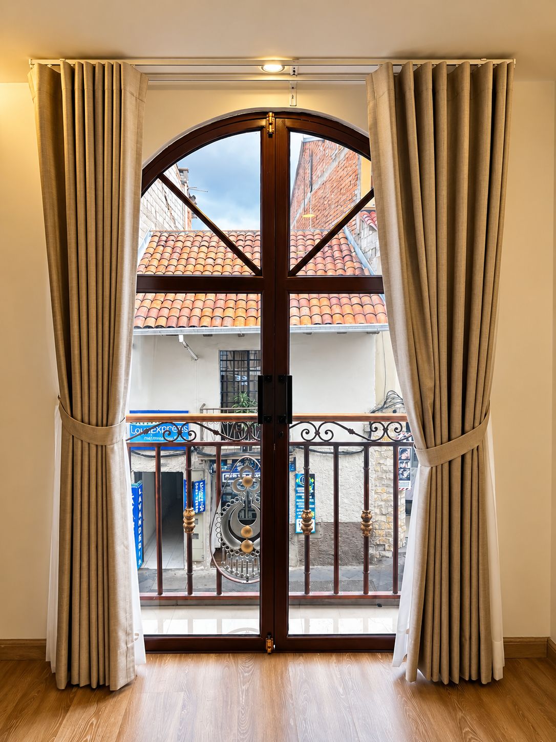 A room with a wooden floor, a large arched door, and beige curtains.