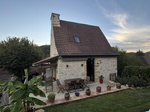 A stone house with a sloped roof, a patio with outdoor furniture, and potted plants. - House with private garden - 4 guests (SAINT POMPON)