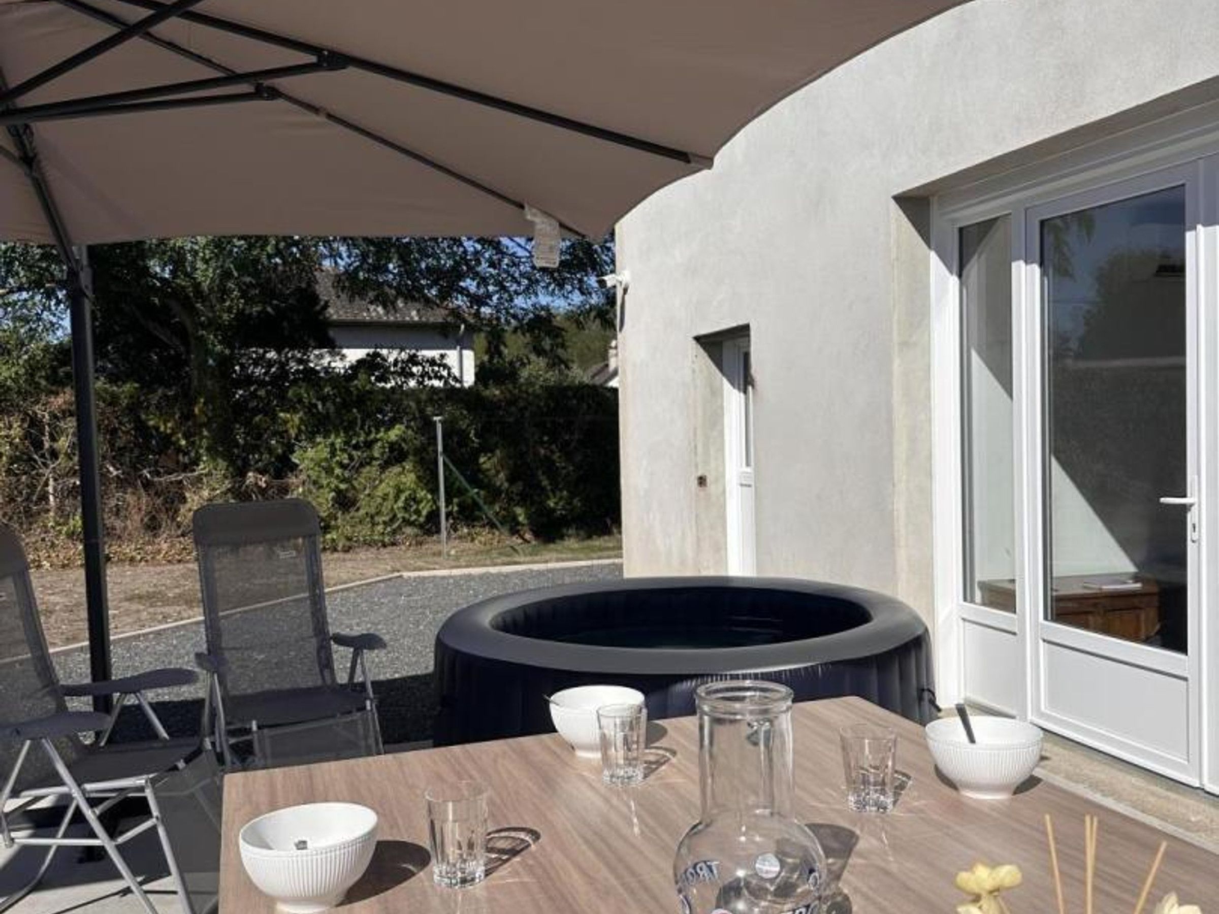 An outdoor dining area with a table set for two, a hot tub, and a covered seating area.