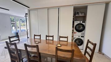 A dining area with a wooden table and chairs, a built-in washing machine unit, and a view through a glass door.