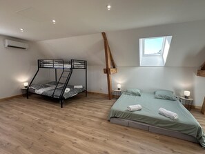 A bedroom with a bunk bed, a single bed, a skylight, and a wooden ceiling beam.