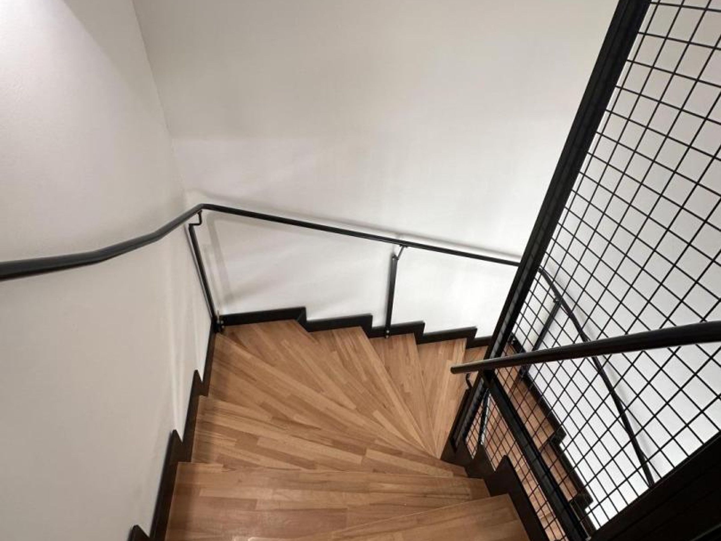 Een houten trap met zwarte leuningen en een wit plafond.