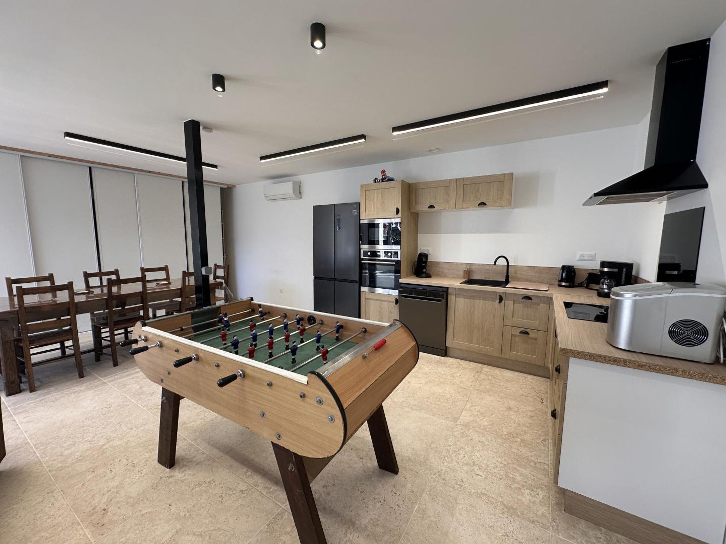 A modern kitchen with a foosball table, a dining area with chairs, and a kitchen island with appliances.