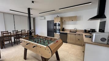 A modern kitchen with a foosball table, a dining area with chairs, and a kitchen island with appliances.