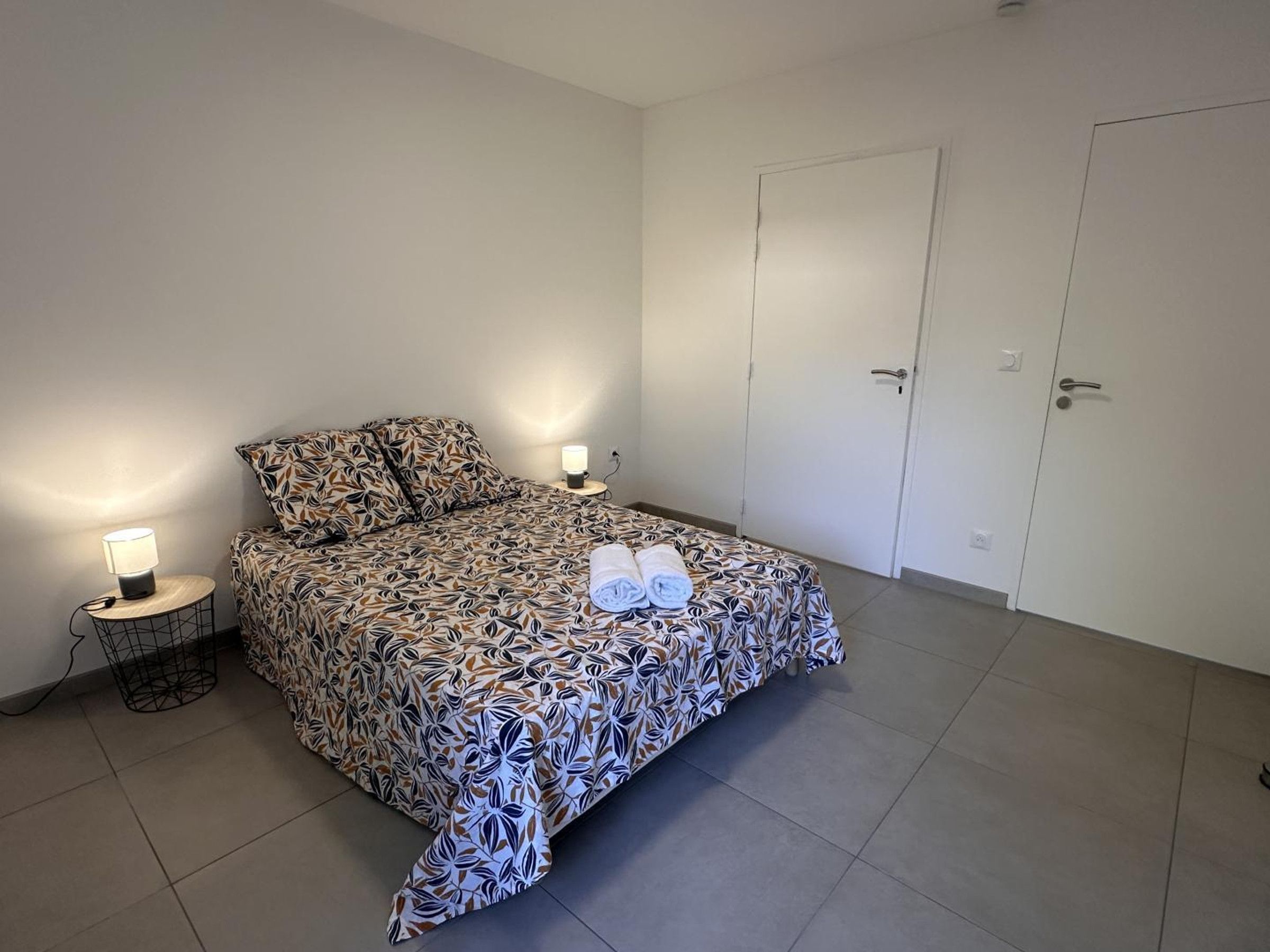 Ett sovrum med ett mönstrat sängöverkast, två sänglampor, en hoprullad handduk och en garderob.